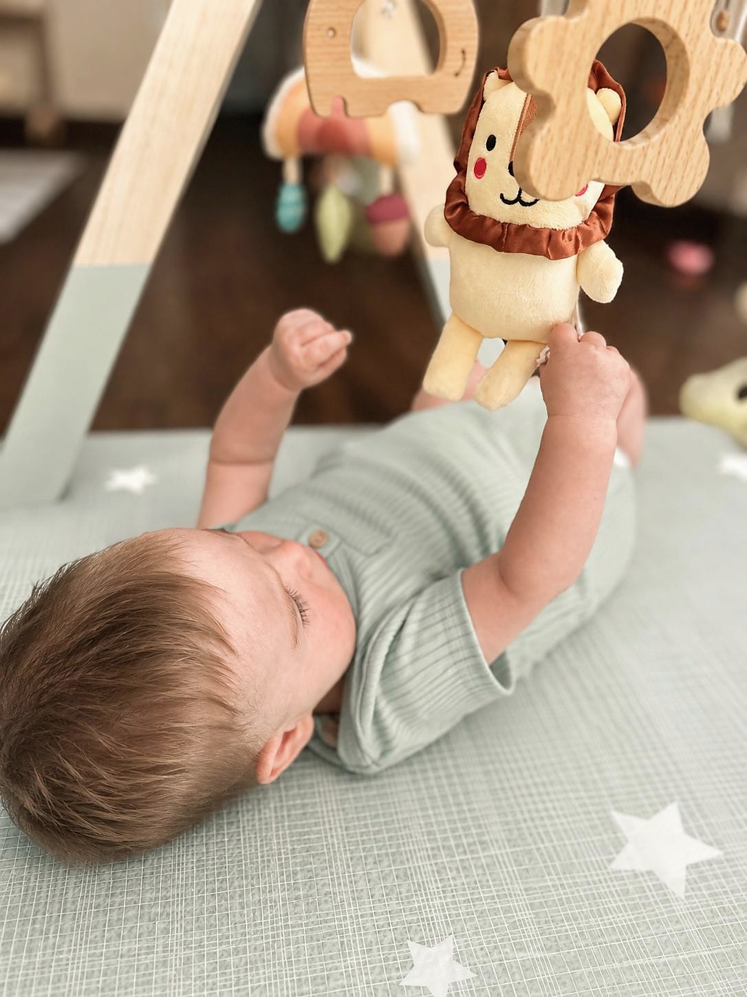An infant reaching toward a wooden hanging toy during floor play at L&L Wicker Park.